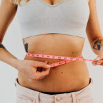 Is Mineral Water Good For Weight Loss Woman in sports bra holding a tape measure on her waist