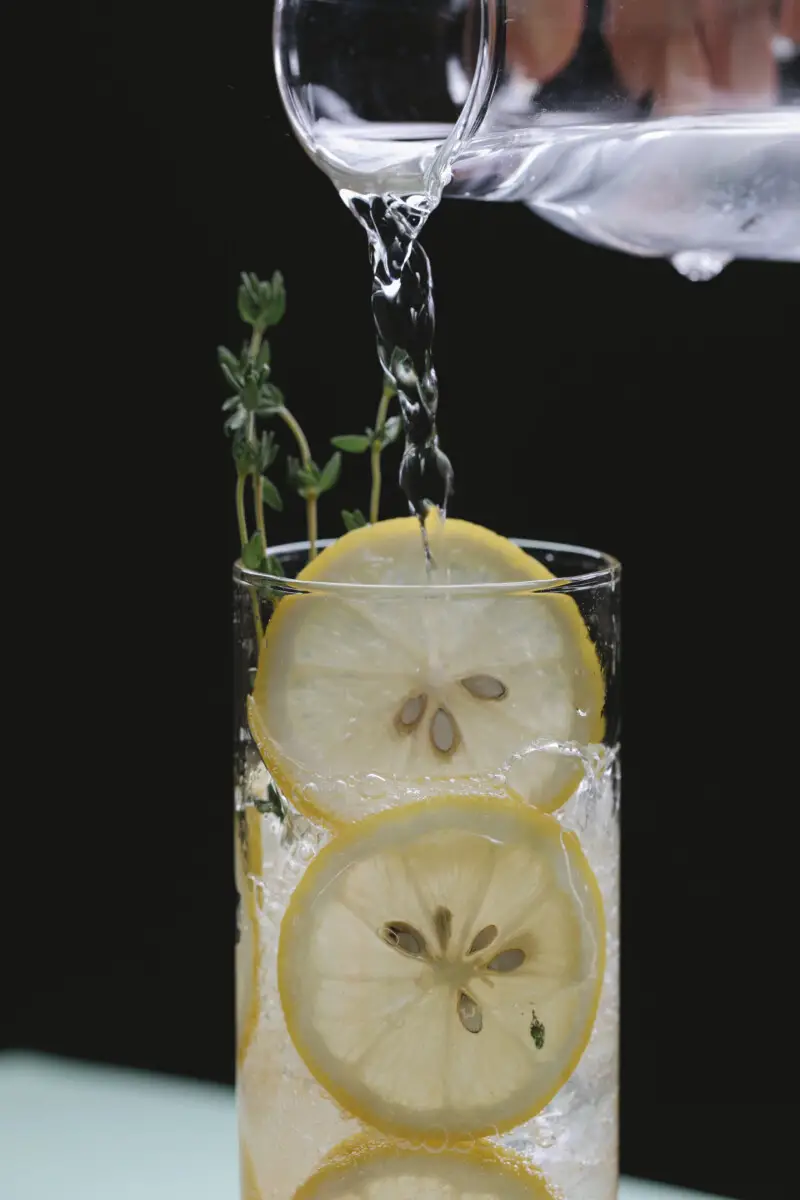 Is Seltzer Water The Same As Tonic Water Person pouring liquid from glass jug into glass with lemon